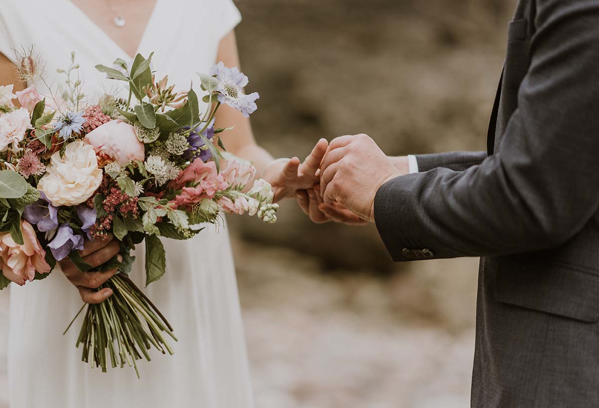 Bride holding vibrant spring wedding bouquet as groom gently holds her hand during an intimate Cape Cod elopement ceremony.