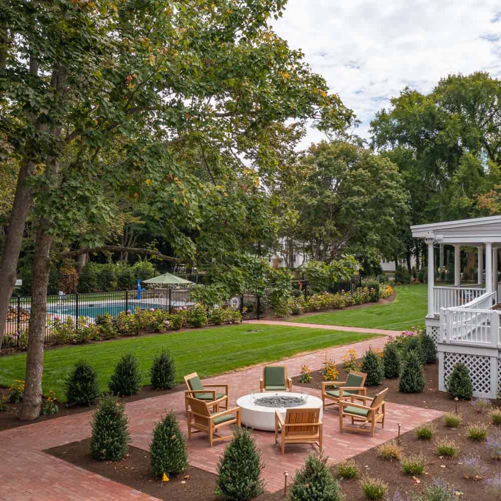 Brick patio firepit with four wooden chairs and landscaped garden at The Charm on Main in Brewster